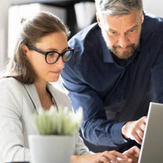 Image d'un homme montrant quelque à une femme sur ordinateur, illustrant le service informatique d'accompagnement proposé par Inibar Services.